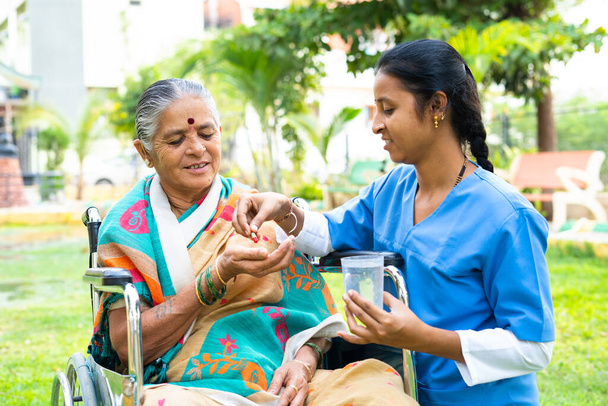 Медсестра дает таблетки или таблетки пожилой женщине на инвалидной коляске - концепция медицинского обслуживания, ухода и лечения - Фото, изображение