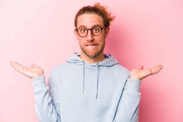 Young caucasian man isolated on pink background confused and doubtful shrugging shoulders to hold a copy space. - Photo, Image