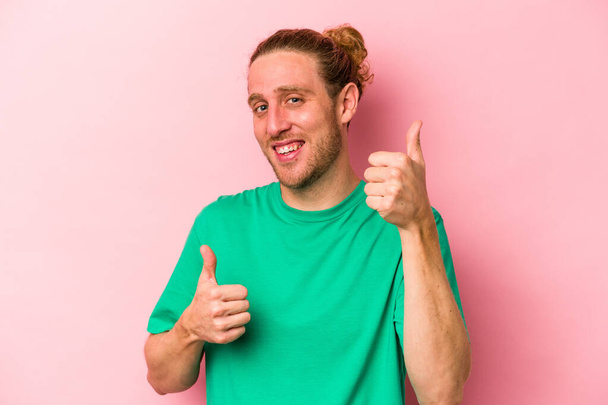 Fiatal fehér férfi elszigetelt rózsaszín háttér emeli mindkét hüvelykujját fel, mosolygós és magabiztos. - Fotó, kép