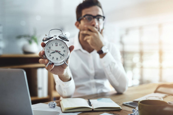Dont let time spiral out of your control. Portrait of a young businessman looking stressed out while holding a clock in an office. - Foto, afbeelding