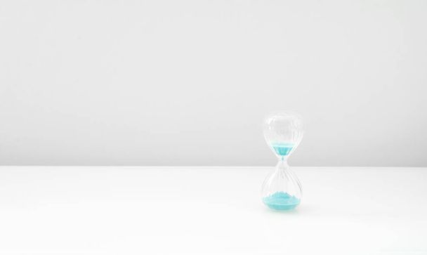 Hourglass on bright light, sandglass with blue sand on white background - Photo, image