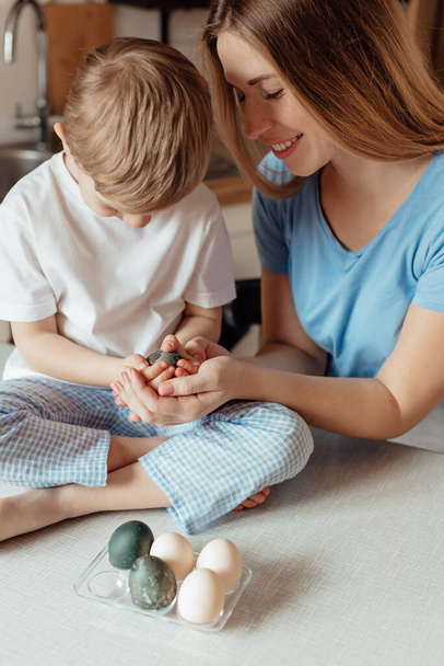 Happy family preparing Easter eggs indoors. Mother and boy celebrating happy Easter holiday together at home. Thanksgiving traditions and childhood togetherness concept. Holiday traditions. Celebration and joy concept. - Photo, Image