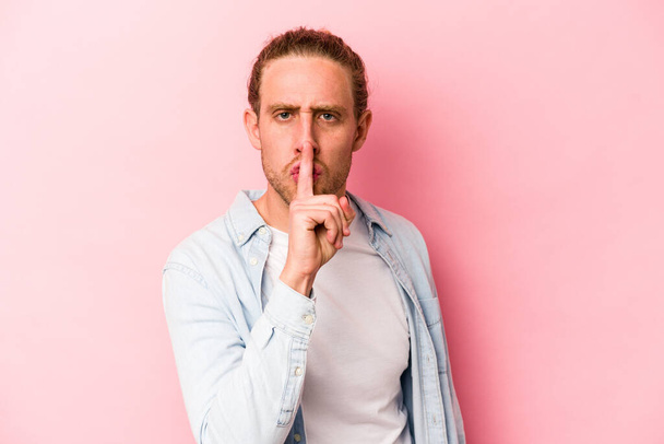 Young caucasian man isolated on pink background keeping a secret or asking for silence. - 写真・画像