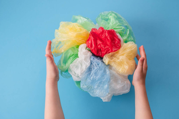 gyermek kezek kezében egy sor műanyag zacskók és műanyag csomagolások különböző színekben egy kék háttér. felülnézet - Fotó, kép