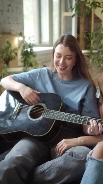 Dvě lgbt dívky sedí ve frontové místnosti na pohovce, hrají na kytaru a zpívají písně, zpomalují. Vysoce kvalitní FullHD záběry - Záběry, video