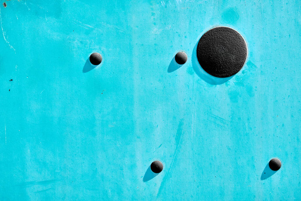 Abstrakt z tyrkysového kovu vyhloubený a pospojovaný životem venku, má 4 malé gumové kroužky a větší černý kruh vrhající mělký stín na dveře. - Fotografie, Obrázek