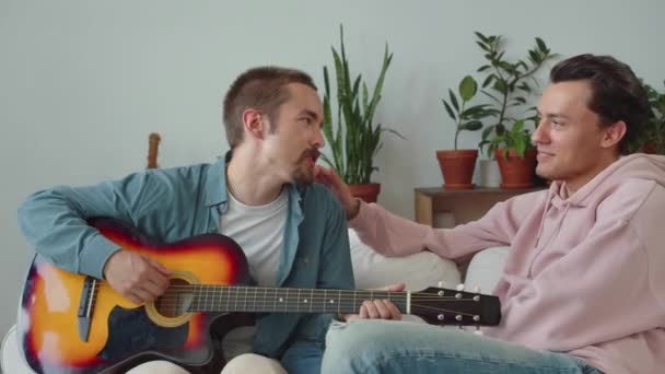 L'un des hommes lgbt montre des compétences de jouer de la guitare à son petit ami et un autre caresse une épaule. Images 4k de haute qualité - Séquence, vidéo