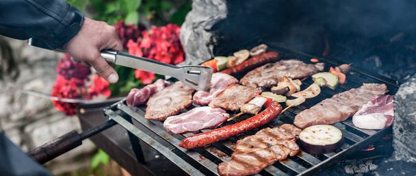 Muž vaří maso na grilu na BQ párty v letní zahradě. Jídlo, lidé a rodinný čas koncept - Fotografie, Obrázek