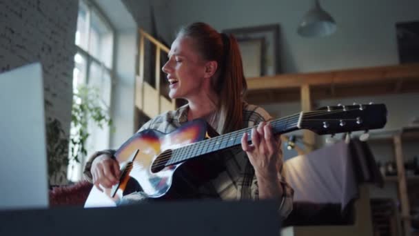 Una mujer adulta se comunica con amigos a través de videollamada. Ella canta expresivamente y toca la guitarra. Imágenes de alta calidad 4k - Metraje, vídeo