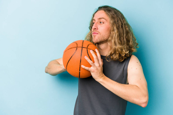 młody biały człowiek gra w koszykówkę odizolowany na niebieskim tle - Zdjęcie, obraz