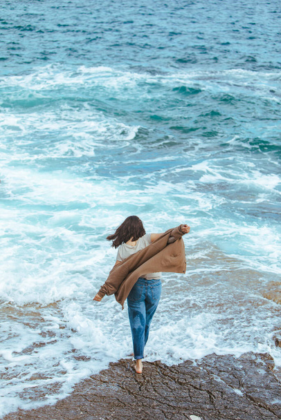 mujer caminando por la playa rocosa en jeans mojados descalza. vacaciones de verano mar
 - Foto, Imagen