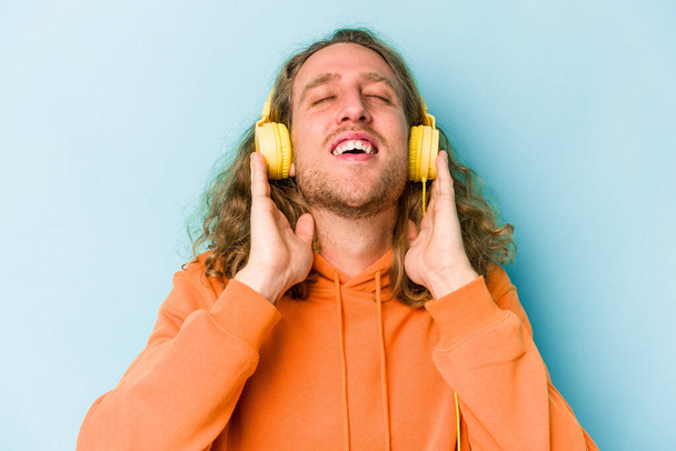 Young caucasian man listening to music isolated on blue background - Fotoğraf, Görsel
