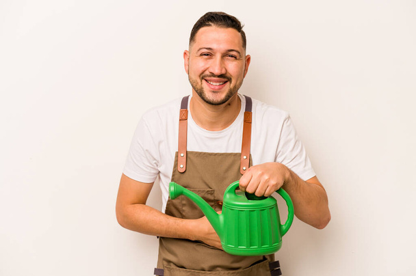 Gardener hispanic man holding a watering can isolated on white background laughing and having fun. - Foto, imagen