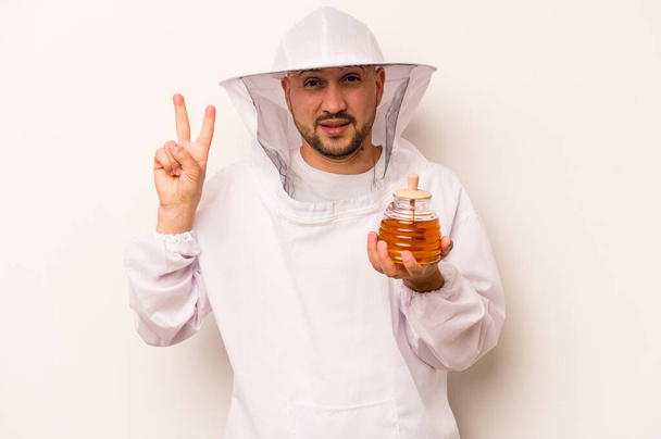 Hispanic beekeeper man holding honey isolated on white background showing number two with fingers. - Foto, Imagem
