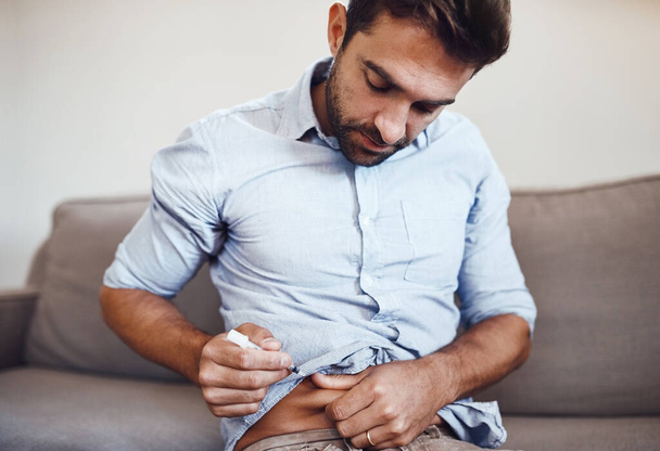 Hes taking good care of himself everyday. Shot of a focused young man taking his daily insulin shot while being seated on a couch at home. - Foto, Imagem