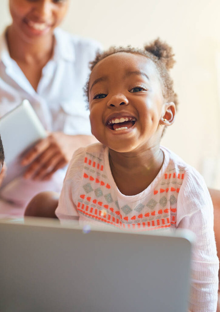 Mucha diversión. Retrato recortado de una adorable niña riéndose mientras juega en una computadora portátil en casa. - Foto, imagen
