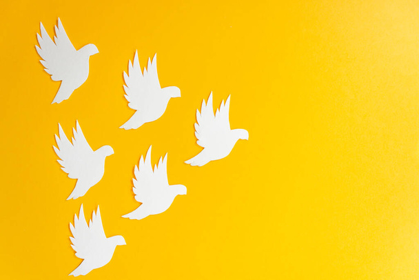 Group of white paper dove birds as a symbol of peace isolated on yellow background. Peace to Ukraine. World Peace Day. - Photo, Image
