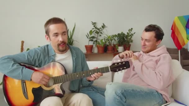 One of lgbt men is showing his boyfriend how to play guitar correctly and another one is listening his attentively. High quality 4k footage - Footage, Video