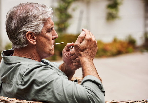 Time to light up. Cropped shot of a relaxed senior man smoking a marijuana joint on his own inside of his garden at home during the day. - Foto, imagen