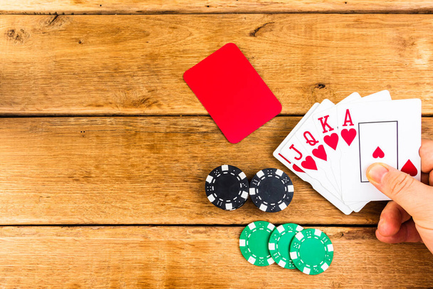 Ruka s královskou flush na dřevěném pozadí, poker žetony, dealer, gambler, poker koncept - Fotografie, Obrázek