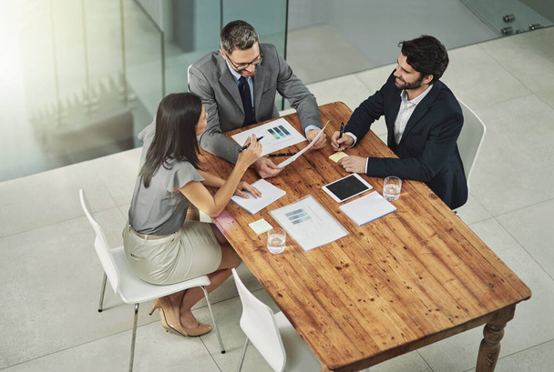 Success their number one priority. Shot of three colleagues sitting around a meeting tablet in the office. - 写真・画像