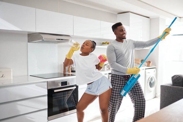 Różnica między zwykłym a nadzwyczajnym jest nieco ekstra. Zdjęcie szczęśliwej młodej pary bawiącej się podczas sprzątania kuchni w domu. - Zdjęcie, obraz