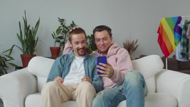 Oturma odasındaki kanepede oturan iki lgbt çekici erkek video görüşmesinde arkadaşlarıyla konuşmaya başlıyor, gülümsüyor ve sohbetin tadını çıkarıyorlar. Yüksek kalite 4k görüntü - Video, Çekim