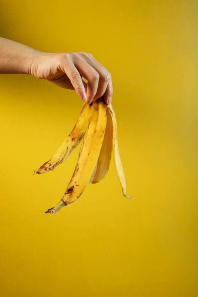 καλλιεργούμενη άποψη του ανθρώπου που κρατά τη φλούδα μπανάνας στο χέρι απομονωμένη σε κίτρινο - Φωτογραφία, εικόνα