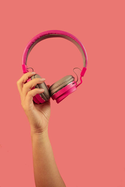 mano sosteniendo auriculares rosados aislados sobre fondo rosa - Foto, Imagen