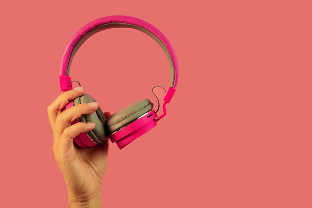 Hand hält rosa Kopfhörer isoliert auf rosa Hintergrund - Foto, Bild