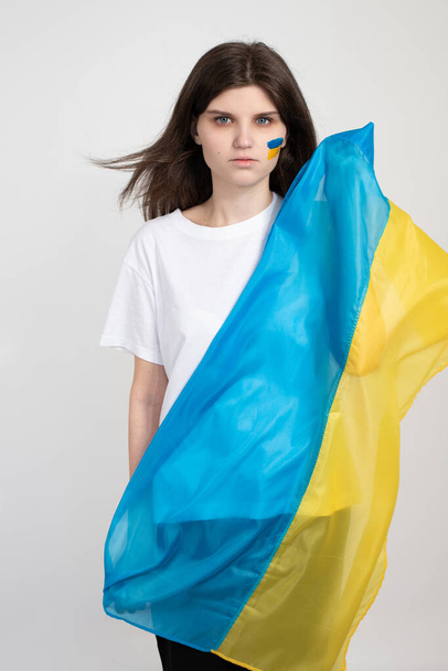 Γυναίκα κρατά ουκρανική μπλε και κίτρινη σημαία σε λευκό φόντο. Το σύμβολο του απαραβίαστου του ουκρανικού λαού. Σταματήστε τον πόλεμο στην Ουκρανία. Η Ρωσία σταματά τον πόλεμο. - Φωτογραφία, εικόνα