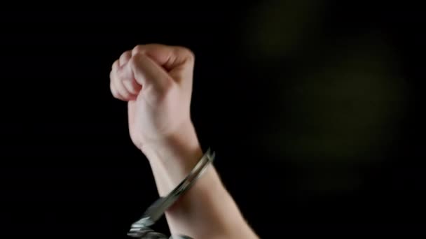 rised fist of caucasian hand shakled in siver handcuffs against black background - Footage, Video