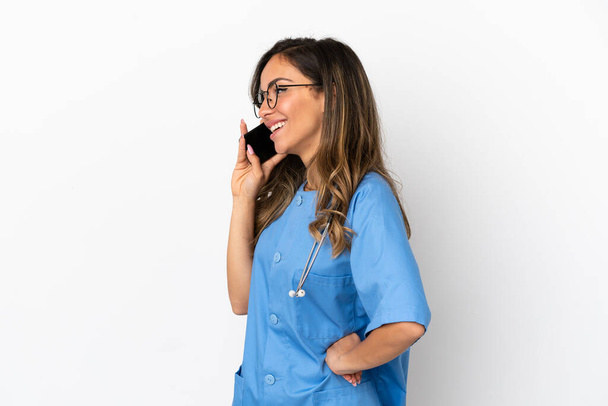 Young surgeon doctor woman over isolated white wall keeping a conversation with the mobile phone with someone - Fotoğraf, Görsel