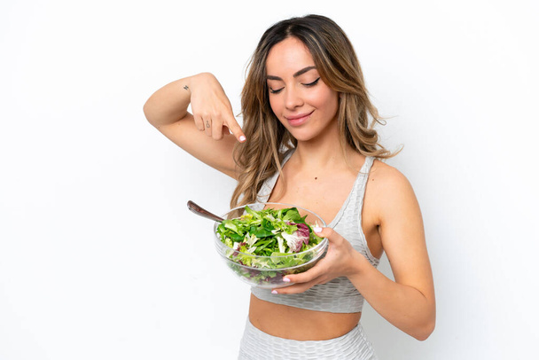 Young caucasian woman isolated on white background with happy expression while pointing a bowl of salad - Fotografie, Obrázek