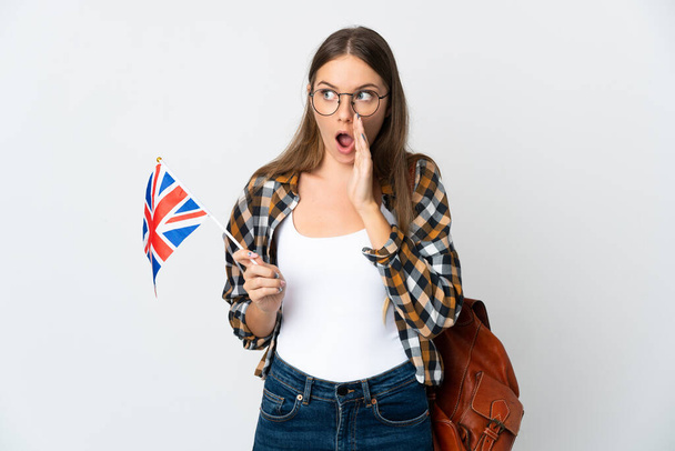 Junge Litauerin mit einer britischen Flagge auf weißem Hintergrund flüstert etwas mit überraschender Geste, während sie zur Seite schaut - Foto, Bild