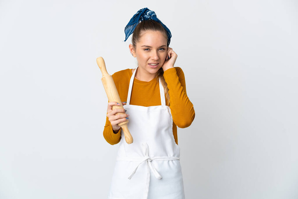 Young Lithuanian woman holding a rolling pin isolated on white background frustrated and covering ears - Photo, Image