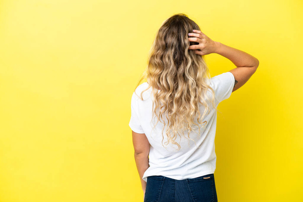 Young Brazilian woman isolated on yellow background in back position and thinking - Photo, image
