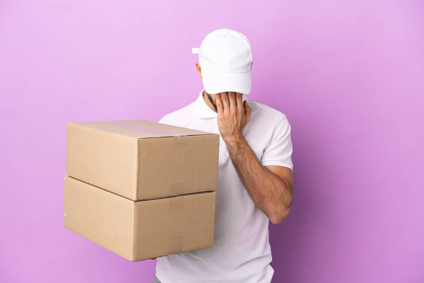 Delivery caucasian man isolated on purple background with tired and sick expression - 写真・画像