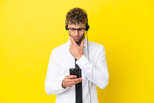 Telemarketer blonde man working with a headset isolated on yellow background thinking and sending a message - Фото, изображение