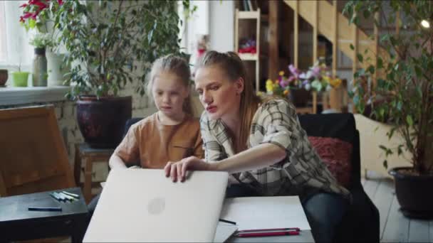 Egy fiatal nő és a lánya egy tágas padláson ülnek. A nő laptopot nyit, hogy rajztippeket találjon. Kiváló minőségű 4k felvételek - Felvétel, videó