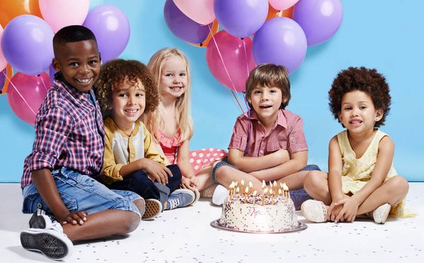 Моє бажання на день народження завжди бути друзями. Знімок групи дітей, що сидять навколо торта на день народження з купою кульок на задньому плані
. - Фото, зображення