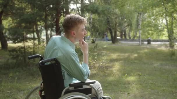 Een jonge gehandicapte man in een blauw shirt zit in de rolstoel, nadenkend en wegkijkend. Hoge kwaliteit 4k beeldmateriaal - Video
