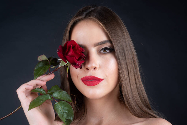 Fashion portrait of young beautiful woman with red rose. Close-up portrait of a beautiful young girl with a rose near face. Unaltered face portrait. Natural skin texture. - Foto, Imagen