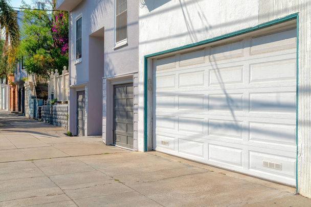 Nachbarschaft mit angeschlossener Garage und Betonauffahrten in San Francisco, Kalifornien. Rechts neben dem grauen Gebäude mit zwei Garagentoren steht ein weißes Haus mit weißem Garagentor. - Foto, Bild