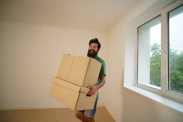 Funny man is carrying his stuff in boxes. Moving to a new apartment. Young happy man with cardboard boxes. Man carrying stacked boxes on moving day. - Foto, Bild
