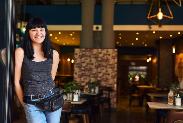 Ready for customers. Shot of a waitress standing at the entrance of a bar. - 写真・画像