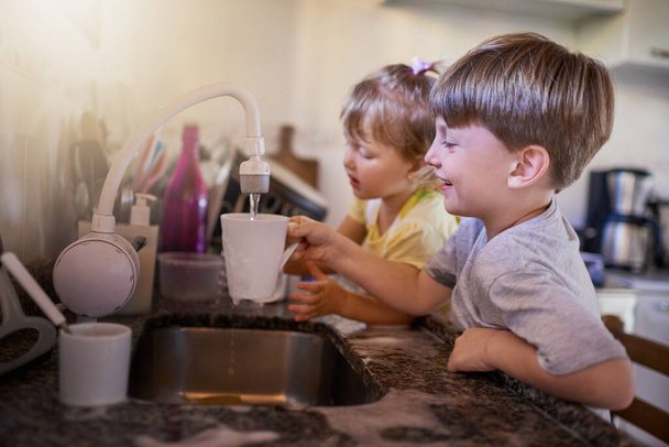 Theyre gonna be super clean when were done. Shot of two adorable little siblings washing dishes together in the kitchen at home. - Fotó, kép