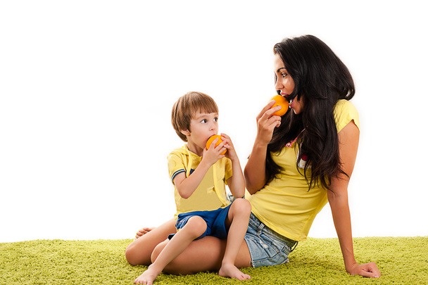 Mother and son eating oranges sitting on green grass - Foto, Imagem