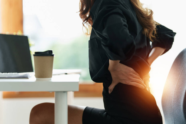 Mujer de negocios asiática sosteniendo su dolor de espalda por exceso de trabajo. Síndrome de oficina. - Foto, imagen
