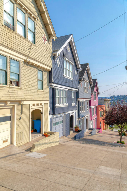 カリフォルニア州サンフランシスコのカラフルな塗装木材の側面を持つ郊外の家。左側の家の前に木のある傾斜コンクリート舗装があります。. - 写真・画像